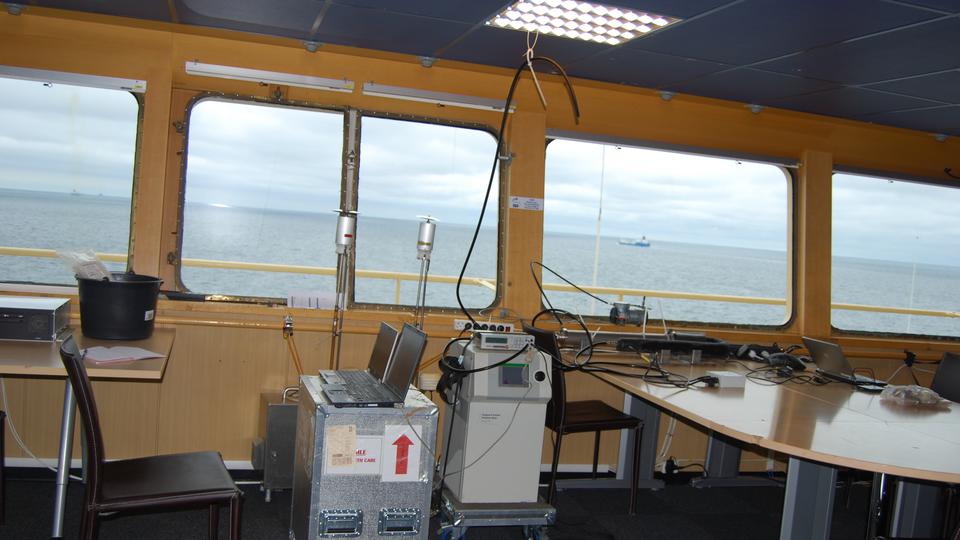 Bild tagen från fartygsbryggan med utsikt genom fönsterventilen. En segelbåt och ett godsfartyg syns på det öppna havet.